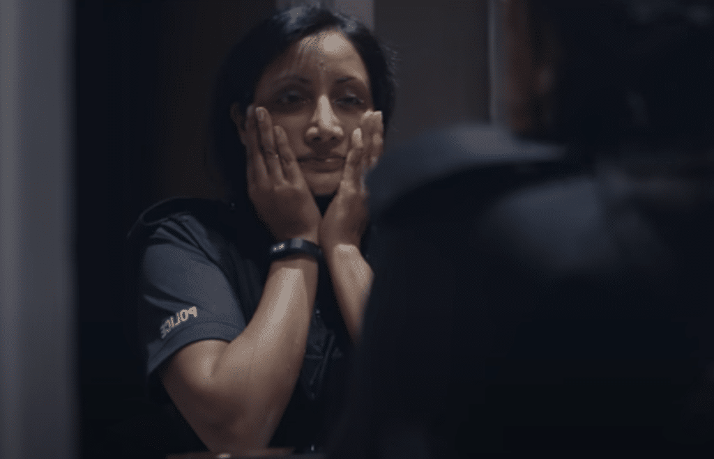 A police officer looking at their reflection, their hand are on their face with worry.